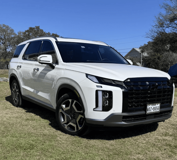 image A white suv parked in the grass near some trees.
