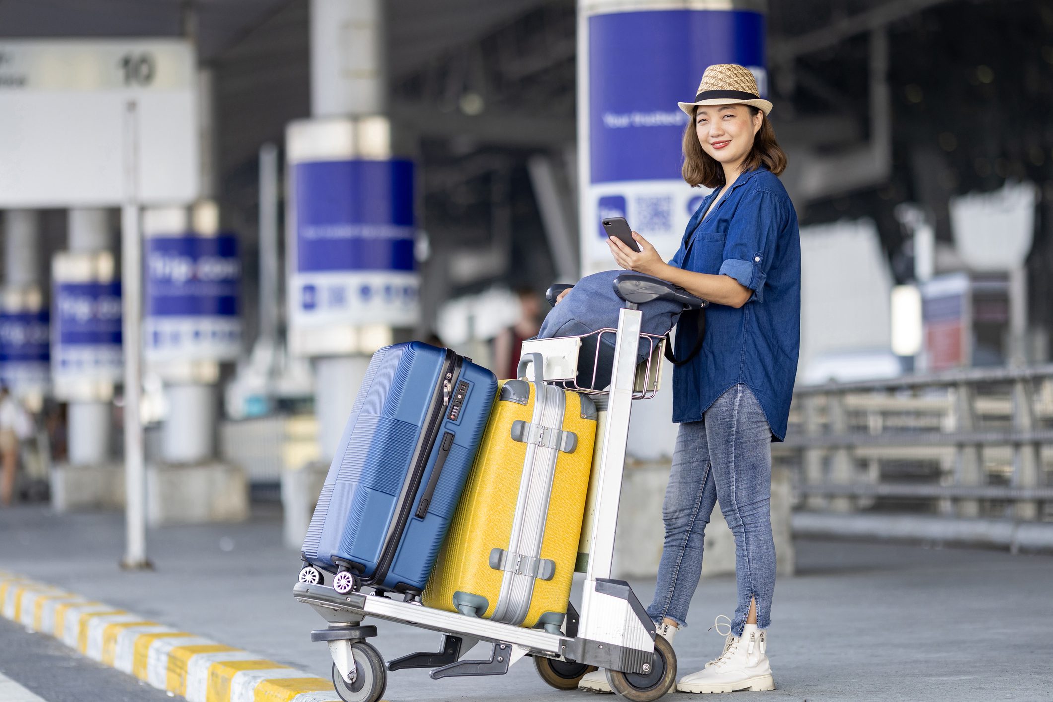 A woman in blue shirt holding luggage on cart.
