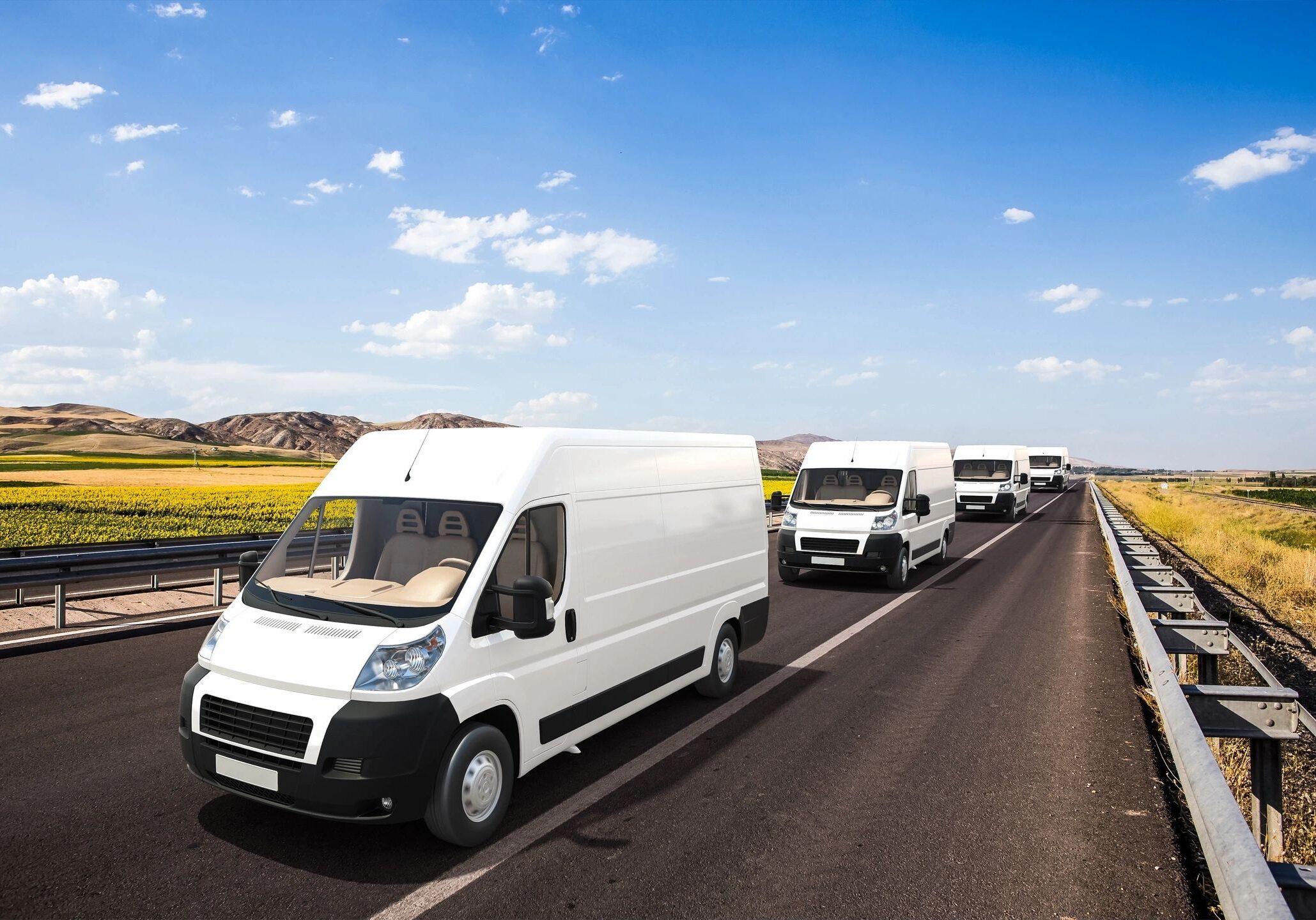 A line of white vans driving down the road.
