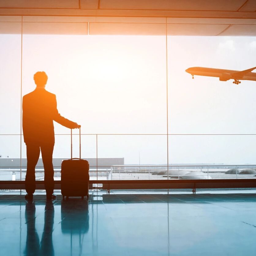 A man standing in front of an airport window with luggage.